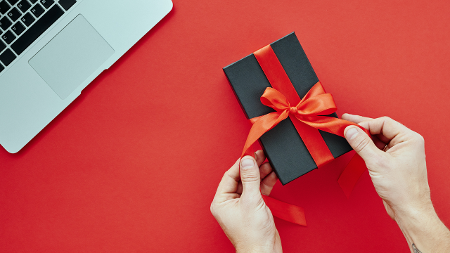 Laptop and small present in red ribbon held by hands