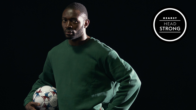 Black man holding football with hand on hip against a black background with Headstrong Logo in top right